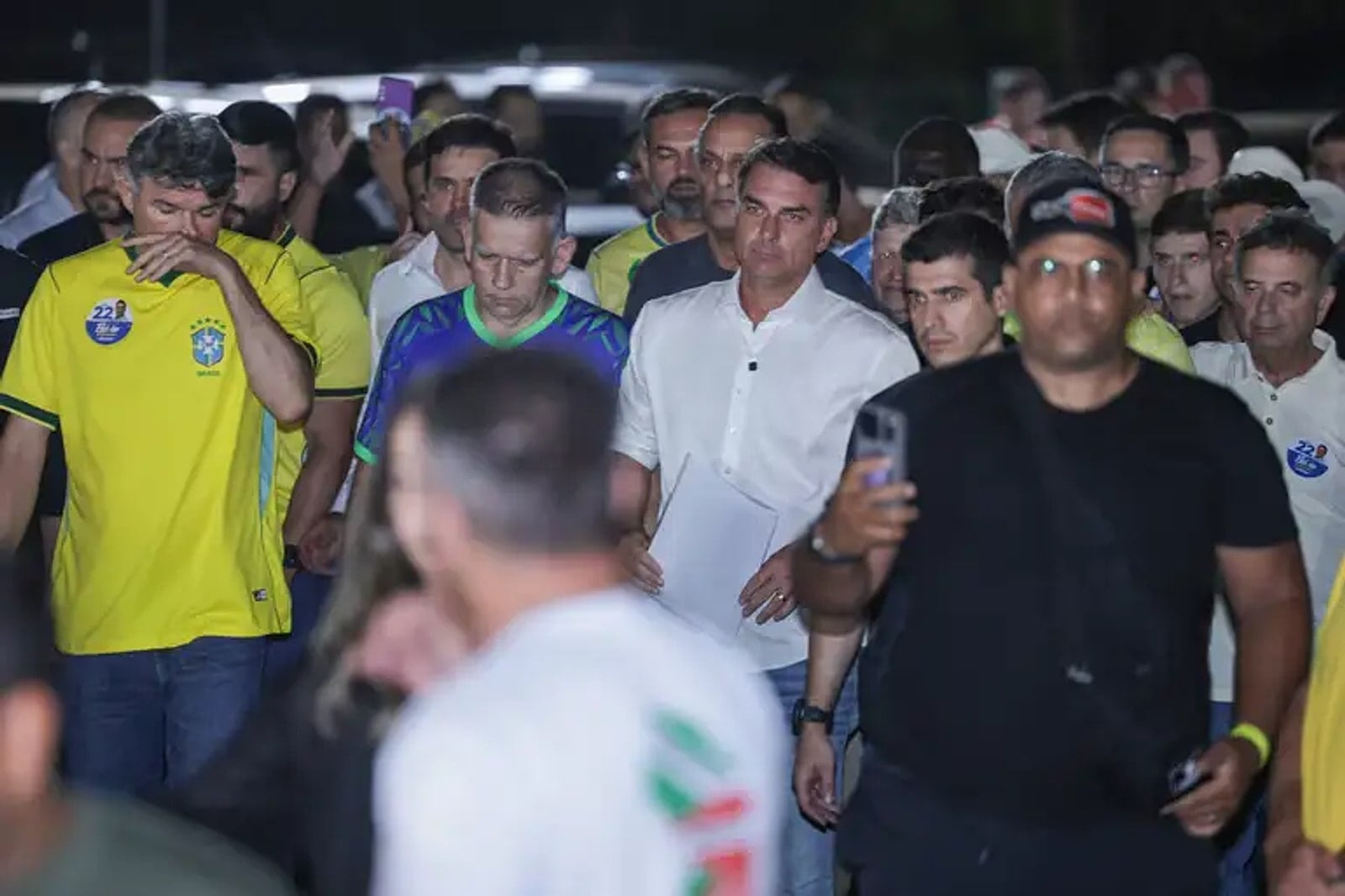 Flávio Bolsonaro caminha cercado de apoiadores e jornalistas.
