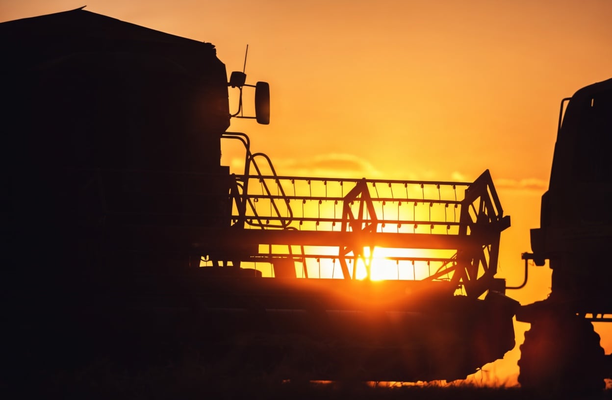 Silhueta de colheitadeira agrícola contra o pôr do sol.