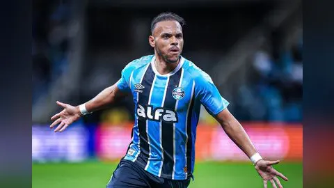 O centroavante Martin Braithwaite, com a camisa do Grêmio, comemora com os braços abertos durante uma partida.