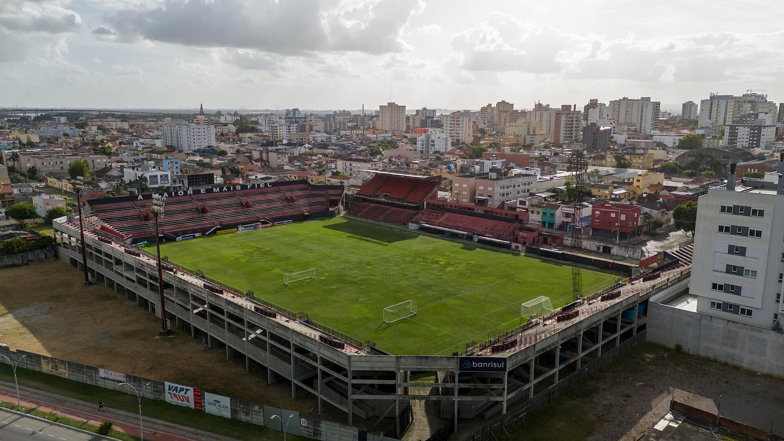 Vista aérea do Estádio Bento Freitas, em Pelotas, com arquibancadas e gramado ao centro e prédios da cidade ao redor.