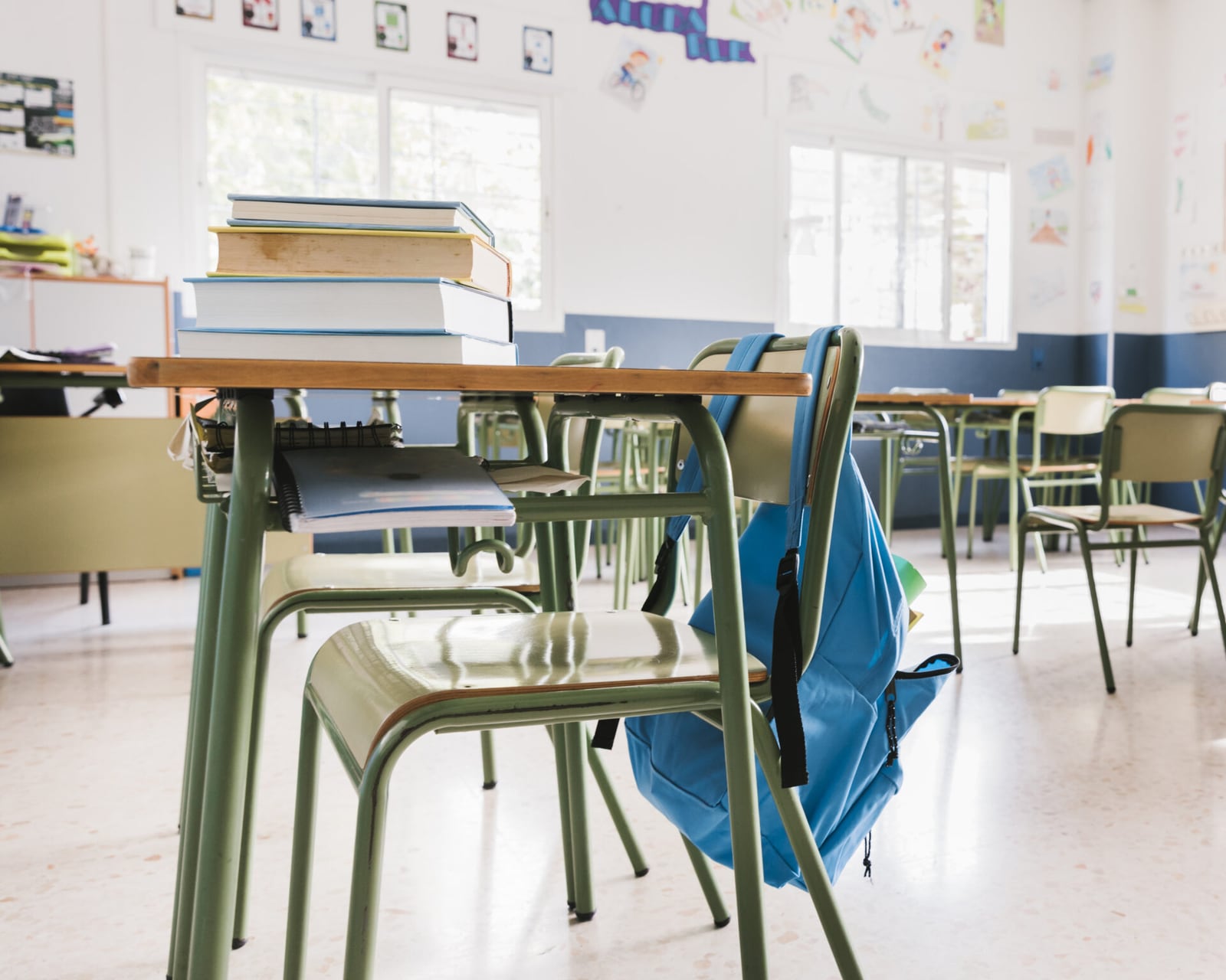 Crianças sentadas em carteiras em sala de aula de escola pública, com professora ao quadro-negro