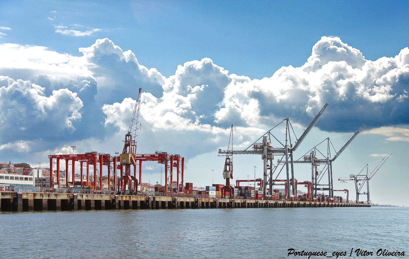 Guindastes e contêineres empilhados no Porto de Lisboa, em Portugal, sob céu com nuvens.