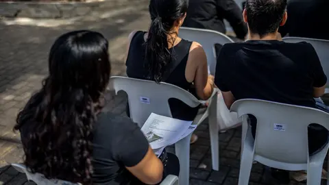 Pessoas conversando em estandes de empresas em um ginásio, com cartazes de vagas de emprego nas mesas