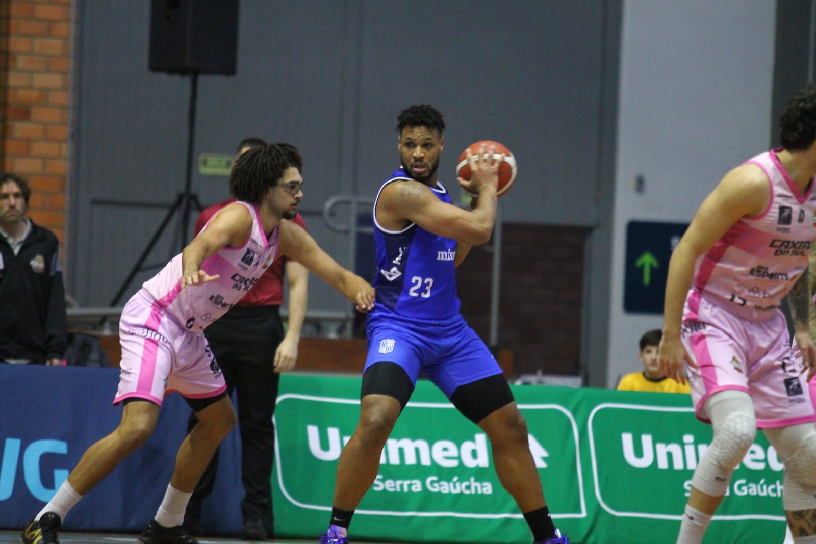 Jogador do Minas, de uniforme azul, com a bola sob marcação de atleta do Caxias, de rosa, durante partida do NBB.