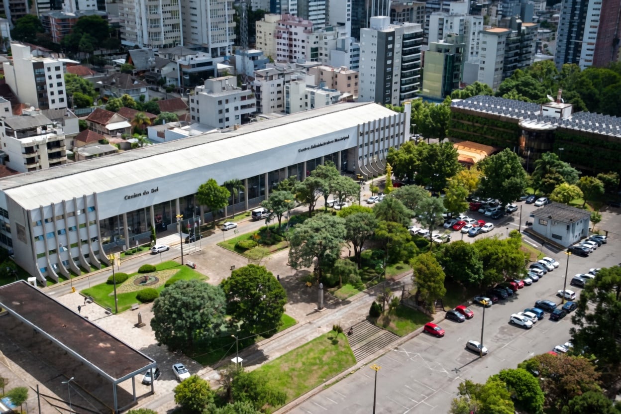 Fachada de prédio público de Caxias do Sul com bandeira do Brasil e movimento discreto de pessoas na entrada