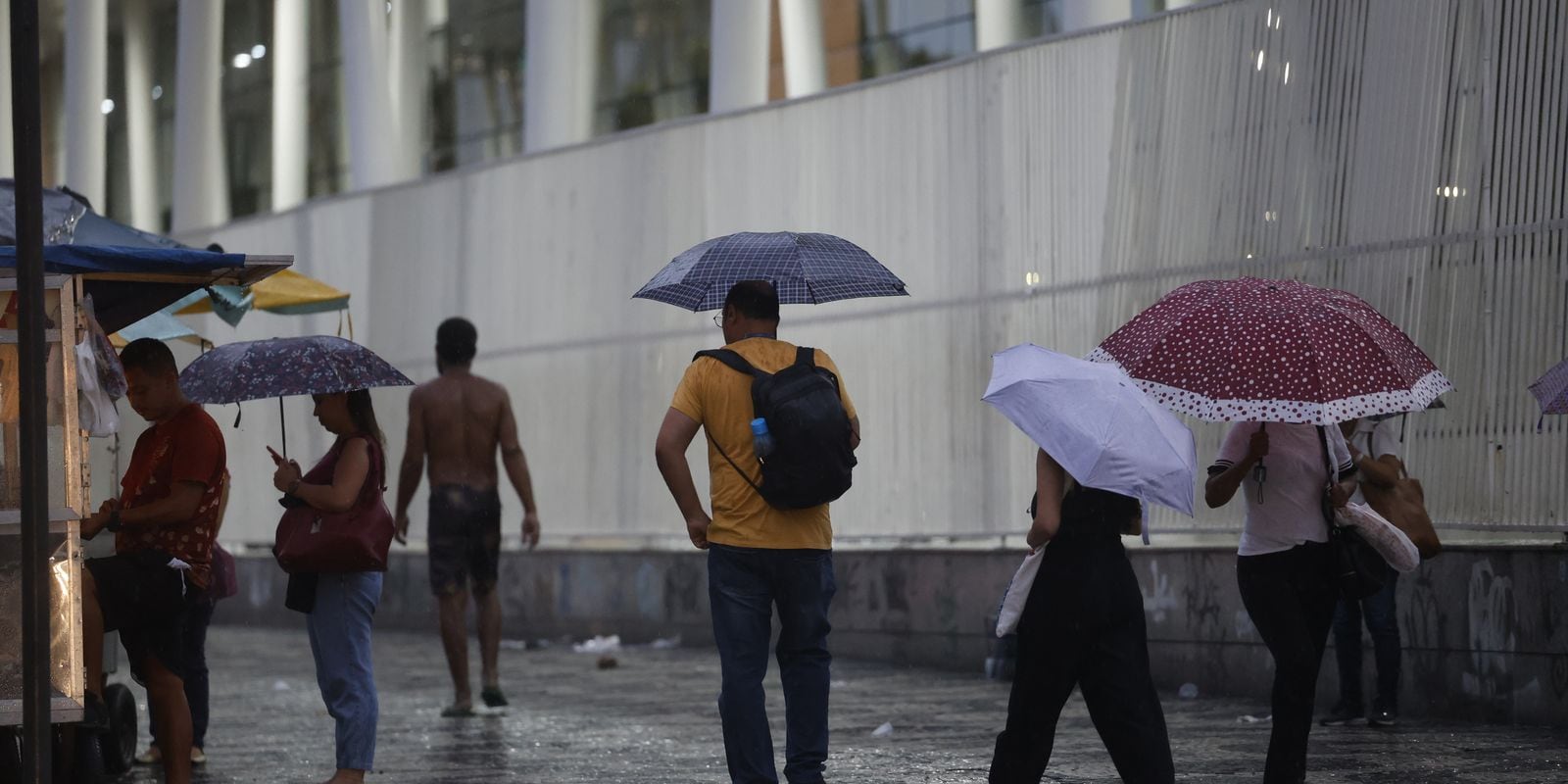 Pedestres se protegem da chuva com guarda-chuvas em uma calçada no Rio de Janeiro.