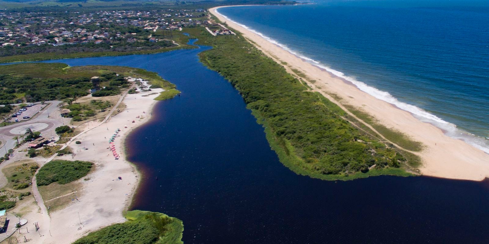 Vista aérea de uma lagoa costeira com faixa de areia e mar ao fundo.