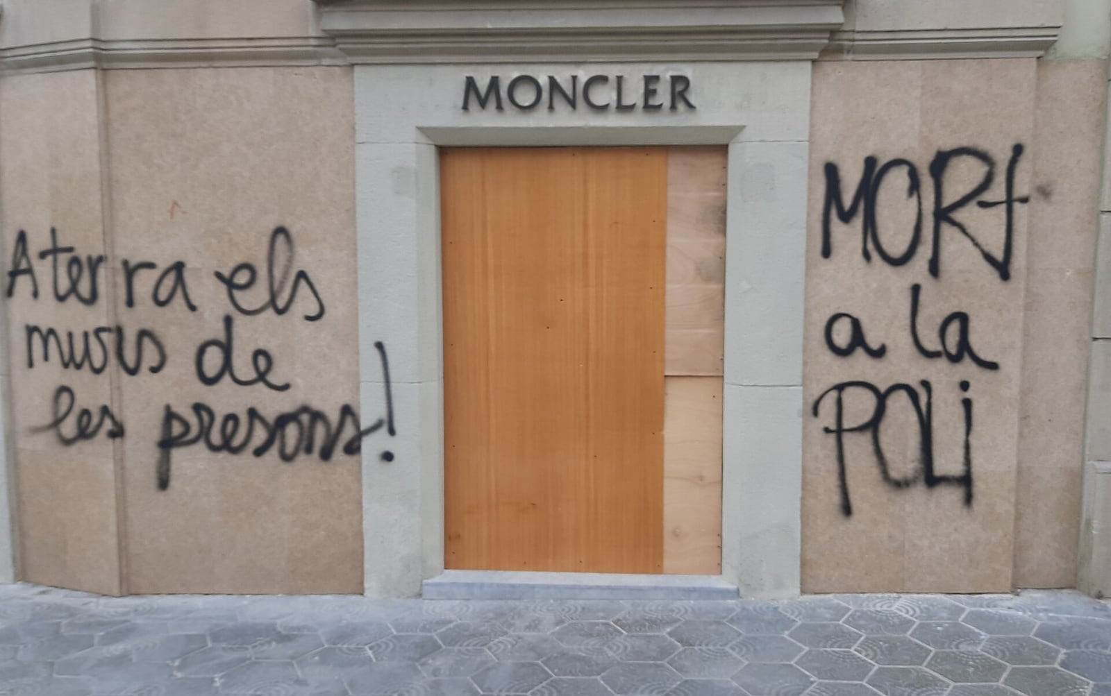 Loja com porta tapada por tapumes e paredes pichadas após distúrbios em Barcelona.