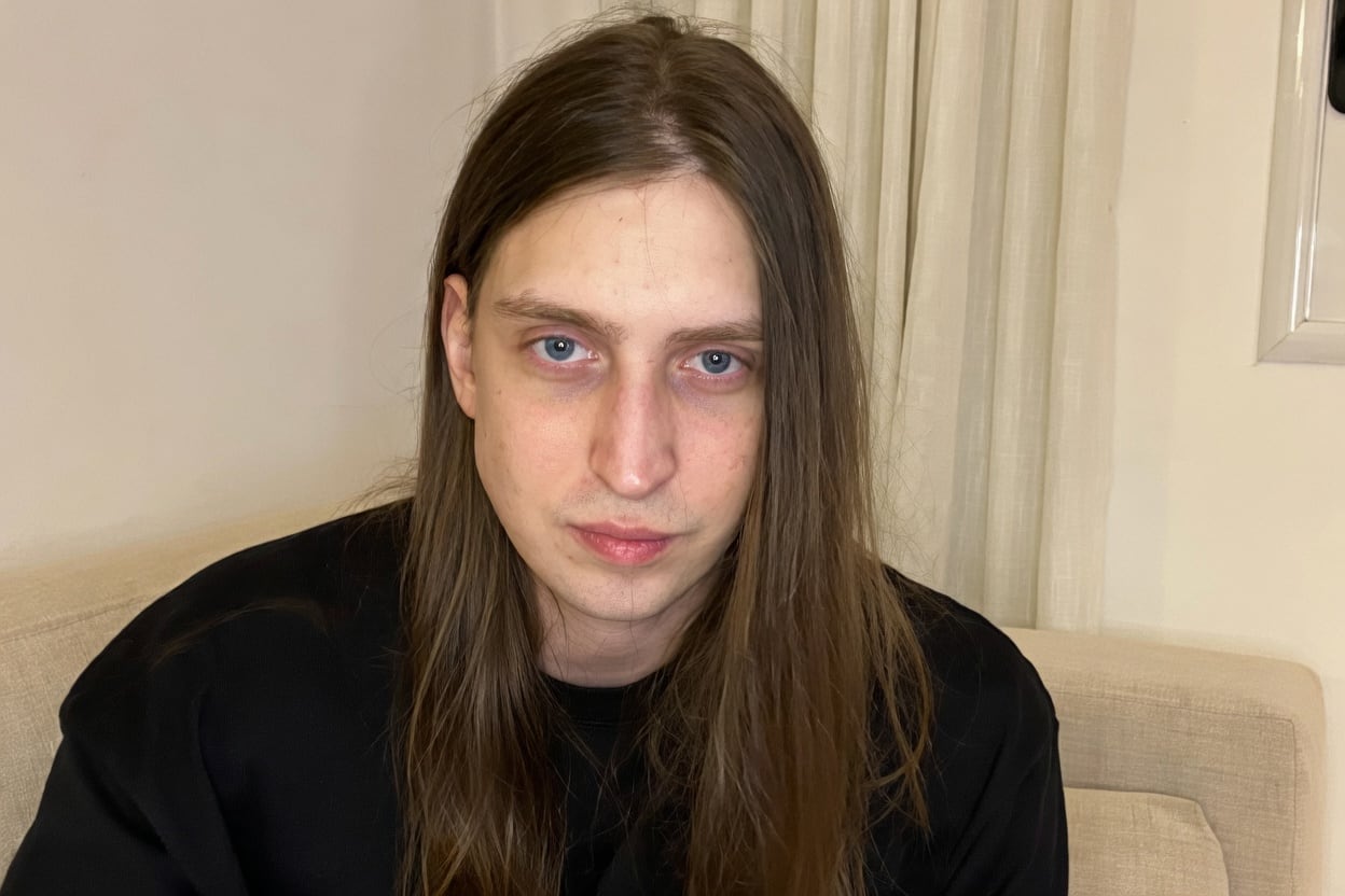O youtuber Felca, de cabelo comprido e camiseta preta, sentado em um sofá em ambiente interno.