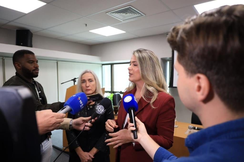 Entrevista à imprensa em sala institucional, com microfones de veículos de comunicação.