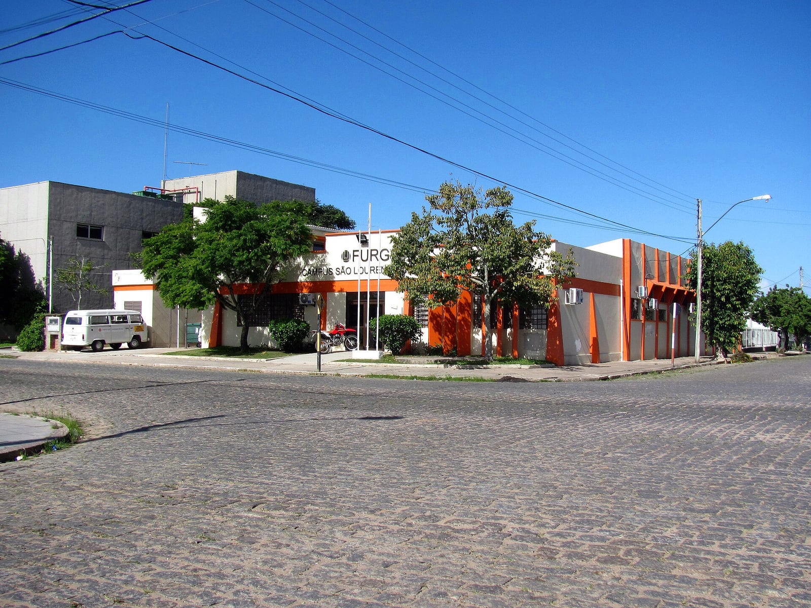 Fachada do Campus São Lourenço do Sul da FURG, com placa da universidade e prédio de cor laranja e branca.