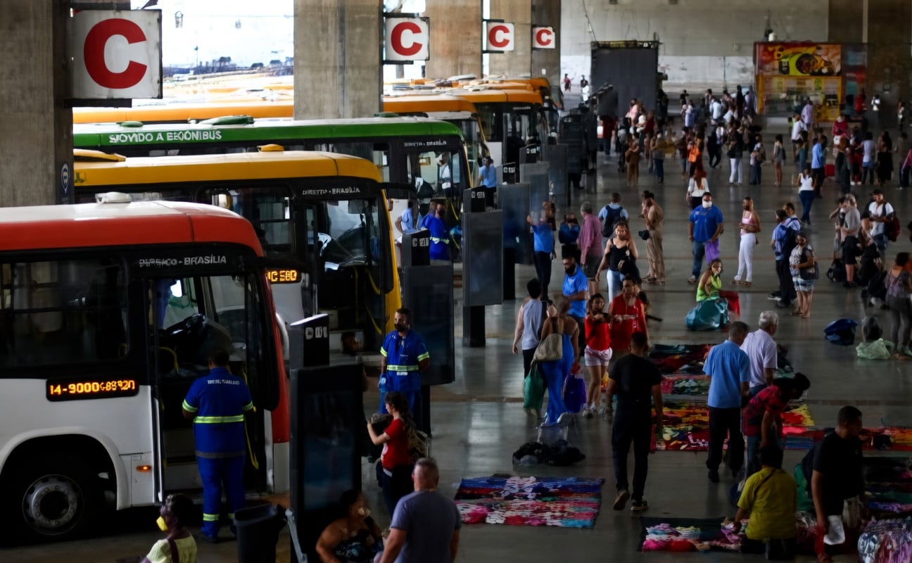 Terminal de ônibus com fluxo de passageiros e veículos do transporte coletivo urbano.