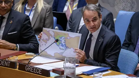 Primeiro-ministro grego Kyriakos Mitsotakis discursa em plenário, com microfone à frente e bandeira ao fundo
