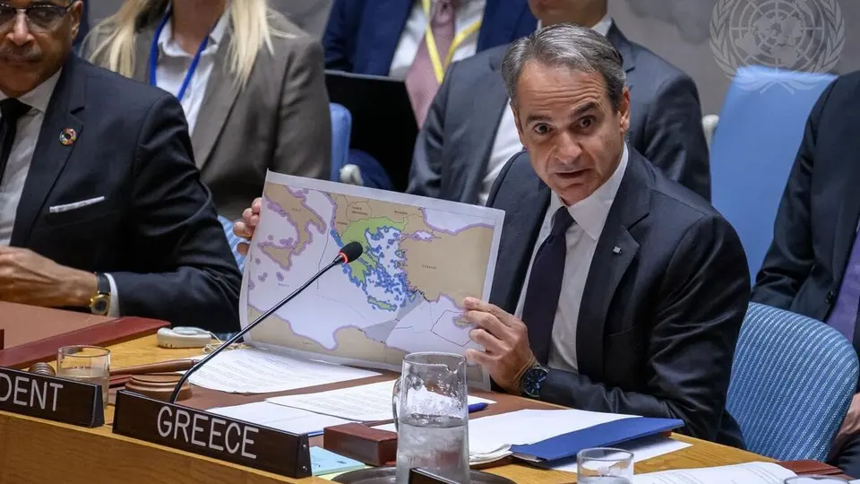 Primeiro-ministro grego Kyriakos Mitsotakis discursa em plenário, com microfone à frente e bandeira ao fundo