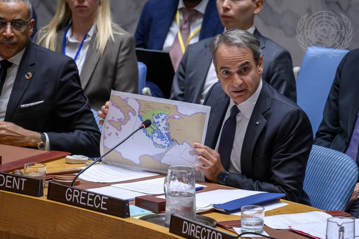 Primeiro-ministro grego Kyriakos Mitsotakis discursa em plenário, com microfone à frente e bandeira ao fundo