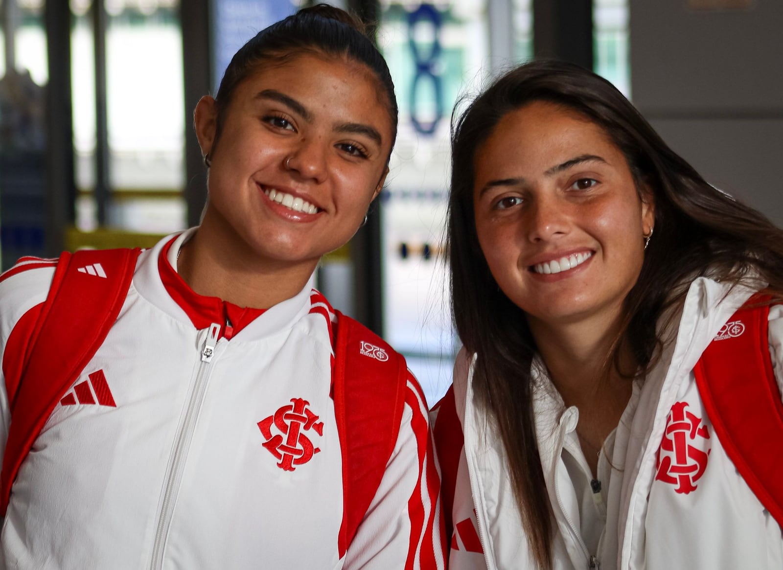 Duas jogadoras do Internacional com agasalho da equipe, sorrindo.