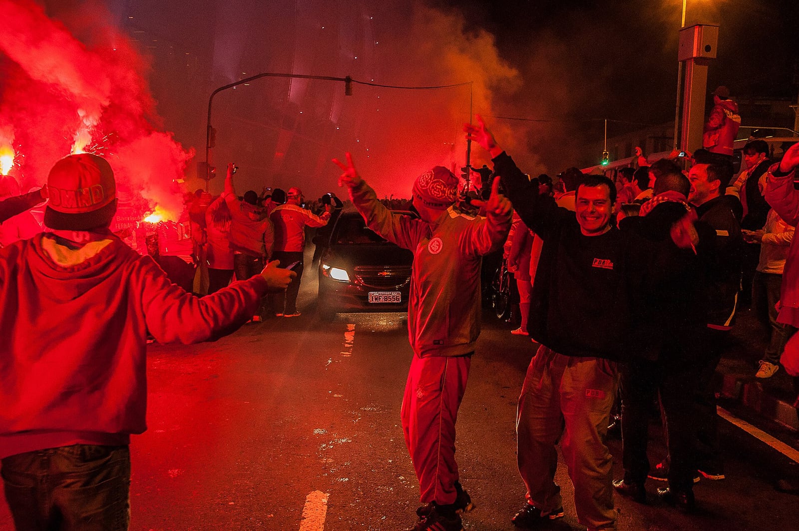 Torcedores do Inter com sinalizadores vermelhos acesos em uma rua de Porto Alegre, em clima de dia de jogo.