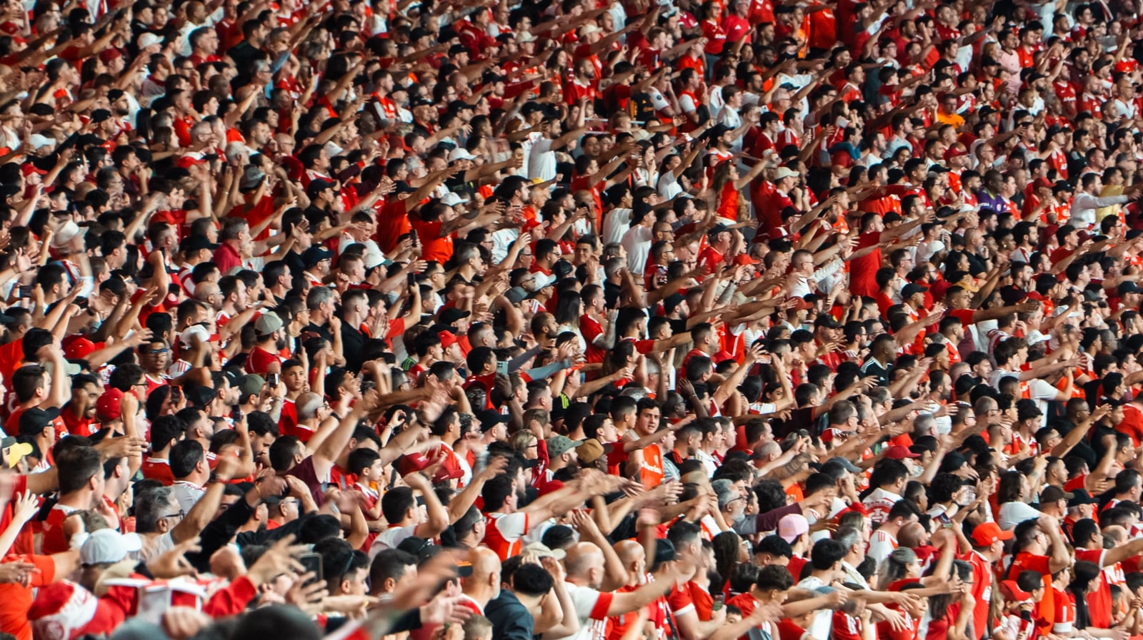 Torcedores do Inter, de vermelho, nas arquibancadas, com os braços levantados.