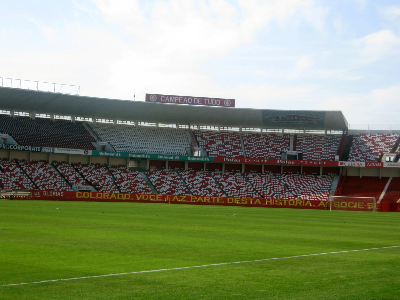 Vista do Estádio Beira-Rio, em Porto Alegre, com arquibancadas vermelhas e brancas e o gramado em primeiro plano.