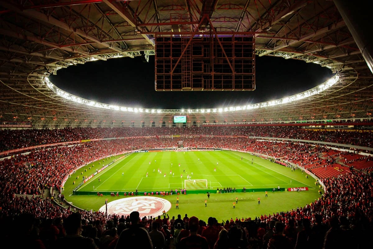 Vista geral do Beira-Rio durante uma partida noturna, com as arquibancadas lotadas e o gramado iluminado.