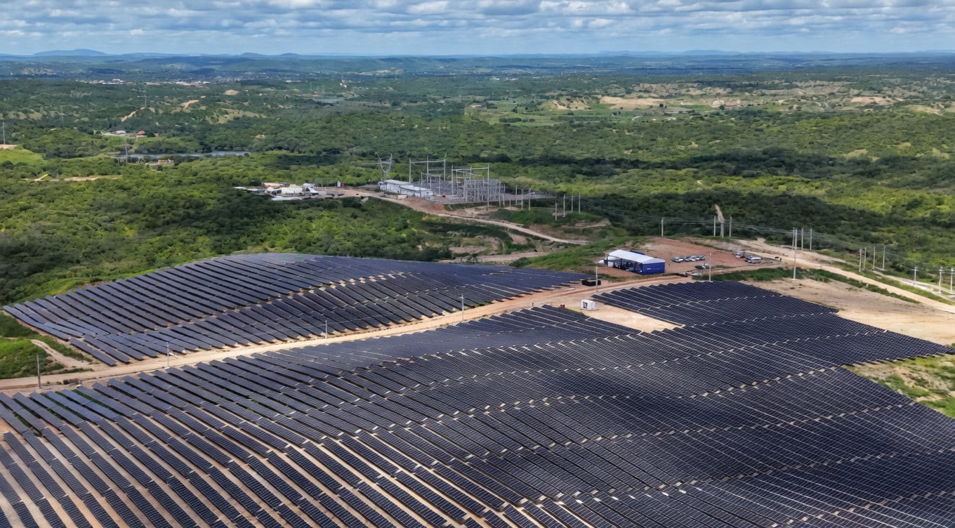 Parque solar com fileiras de painéis fotovoltaicos em área de vegetação, com subestação de energia ao fundo.