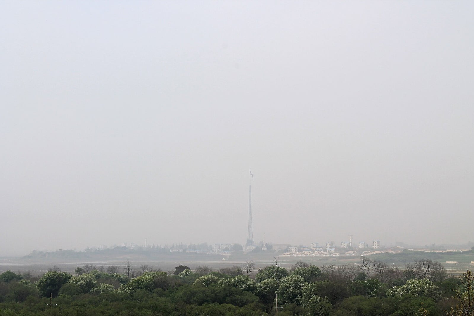 Vista de um povoado e de um mastro de bandeira do lado norte-coreano da fronteira, sob forte névoa.