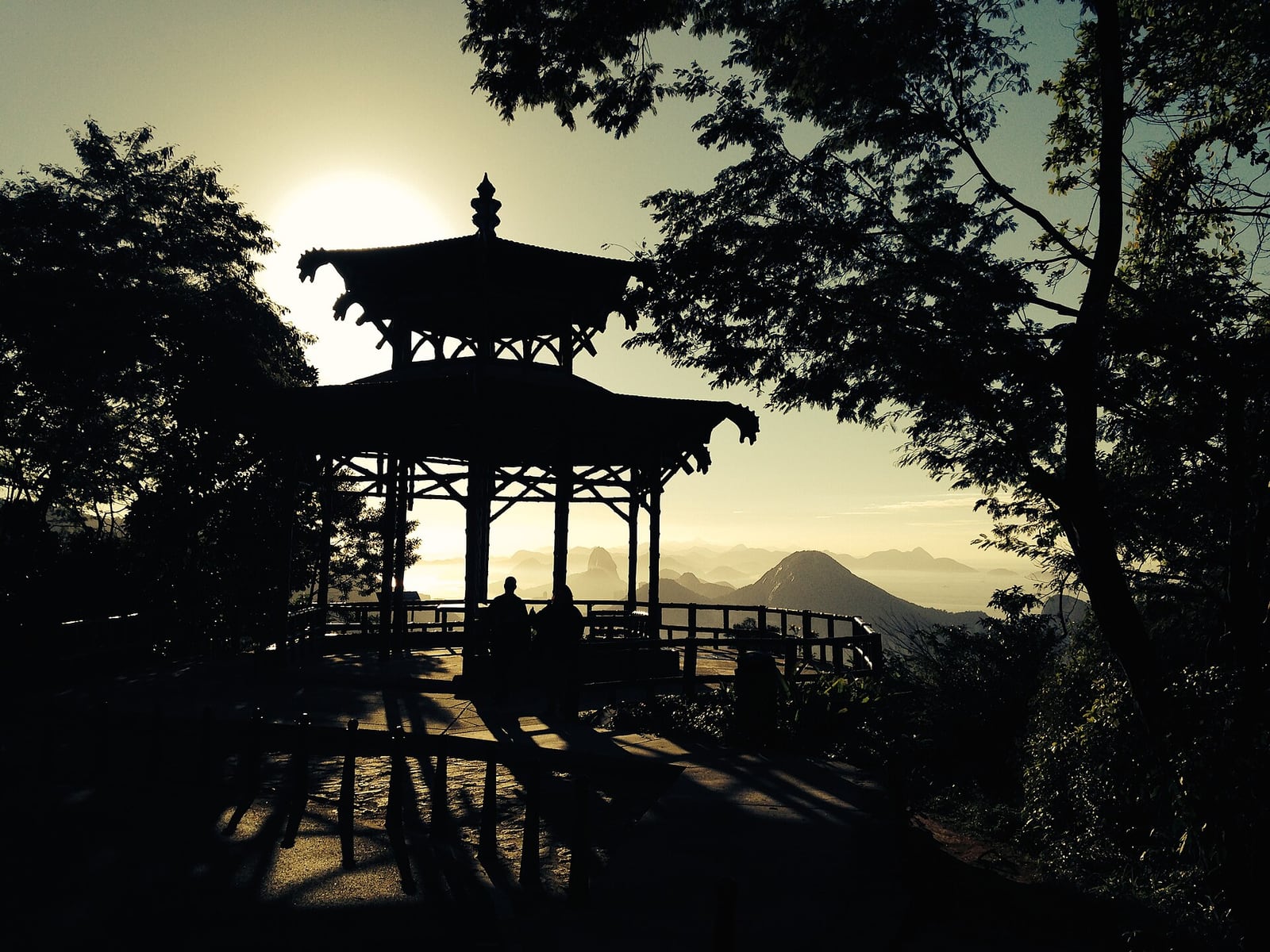 Mirante da Vista Chinesa, na Floresta da Tijuca, Rio de Janeiro, ao entardecer, com silhuetas de visitantes e vista para a cidade.
