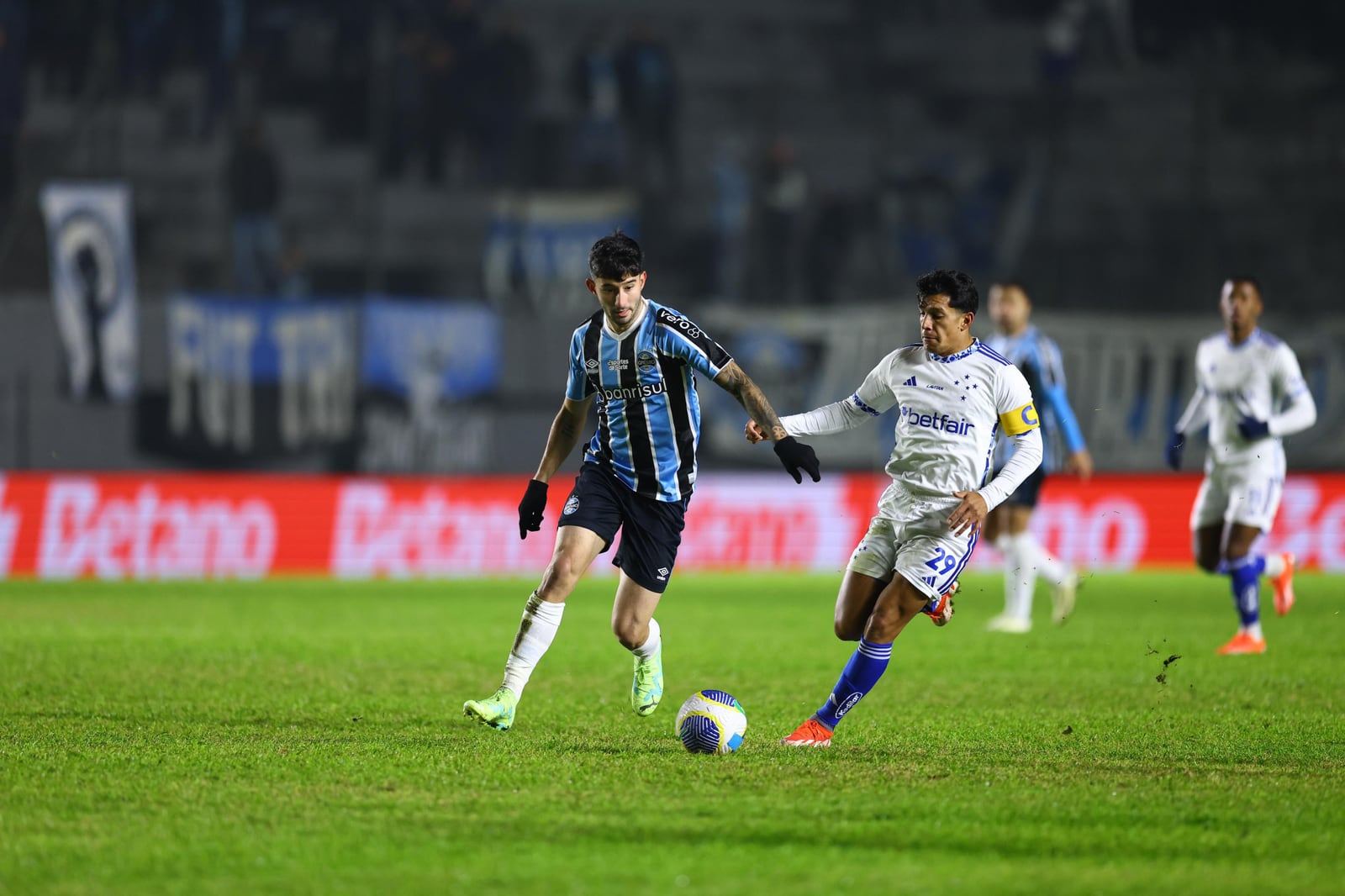 Jogador do Grêmio e jogador do Cruzeiro disputam a bola durante partida do Campeonato Brasileiro.