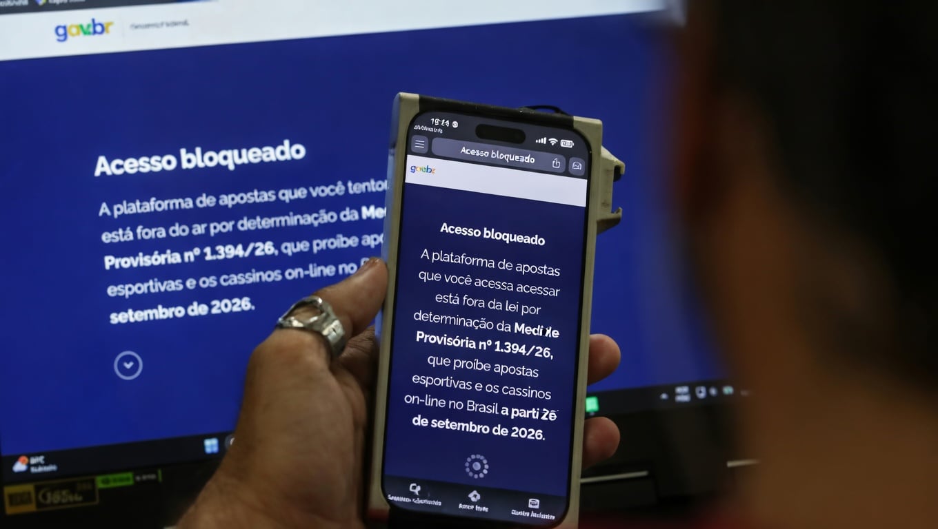 Celular diante de tela com aviso de acesso bloqueado a uma plataforma de apostas online.