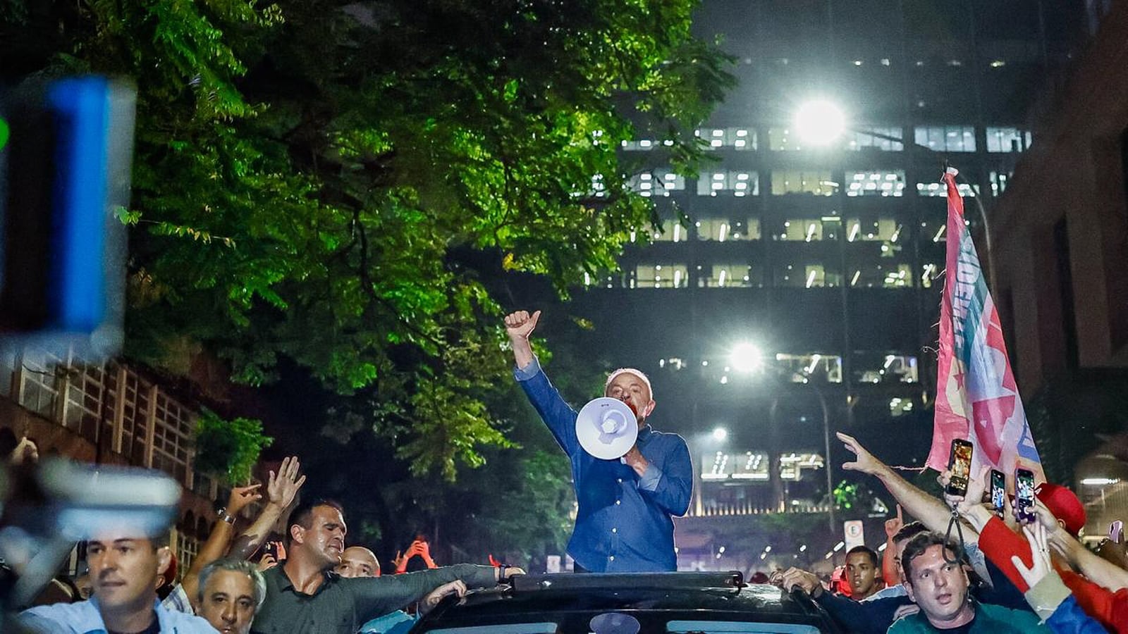 Lula discursa de cima de um carro, com megafone, cercado por apoiadores. Foto de 26/10/2026.