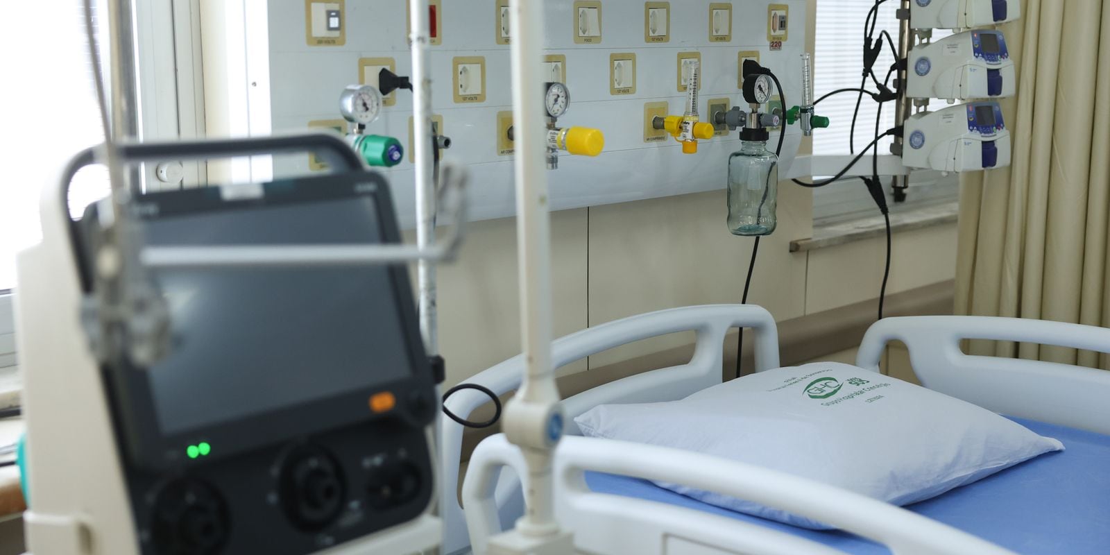 Leito de UTI com monitor, tubulações de oxigênio e bombas de infusão.