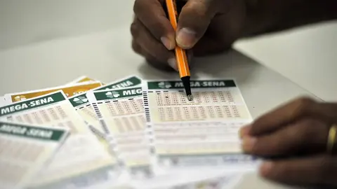 Lotérica com cartões de apostas da Mega-Sena sobre o balcão e volante marcado com números