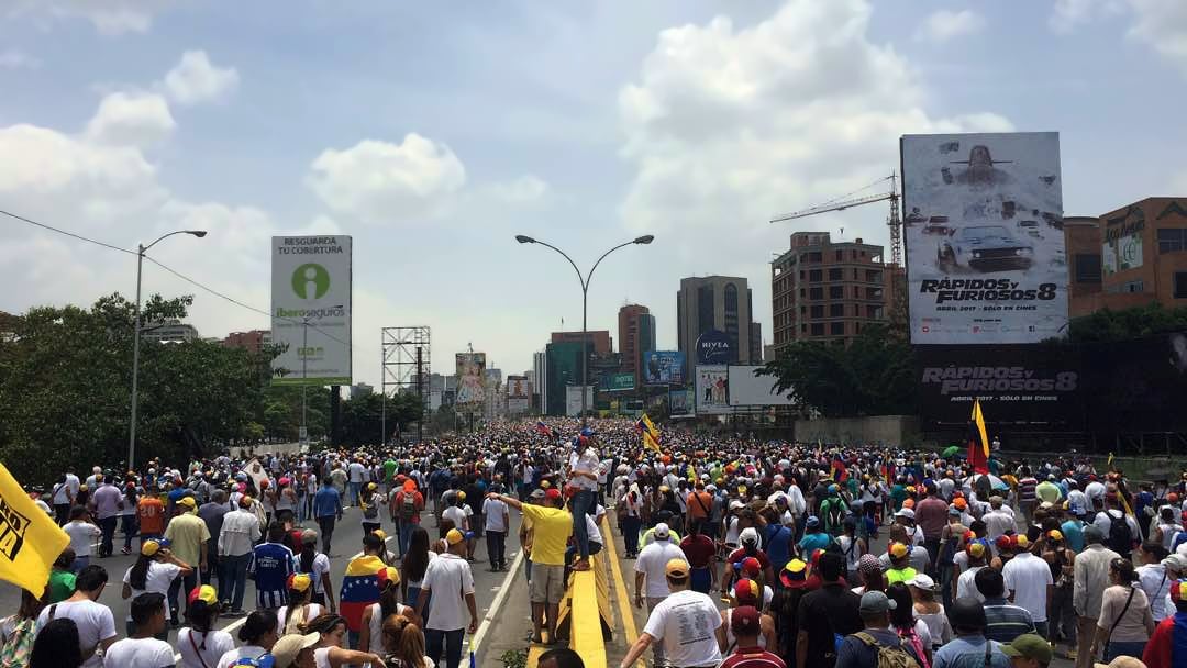 Multidão de manifestantes em uma avenida de Caracas, com bandeiras da Venezuela, durante protesto da oposição.