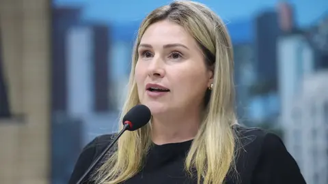 Vereadora de camiseta rosa conversando com colegas durante sessão plenária na Câmara Municipal de Novo Hamburgo