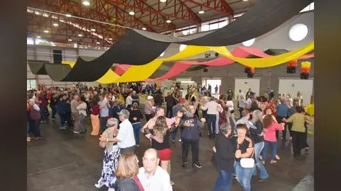 Público dança em salão decorado com faixas nas cores da bandeira alemã durante a Oktoberfest Erechim 2025.