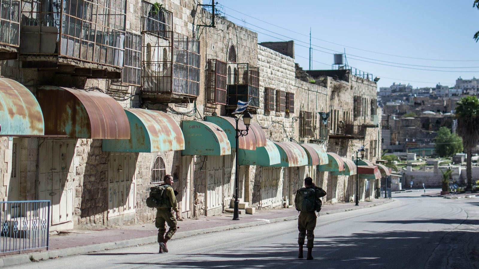 Soldados israelenses patrulham uma rua de Hebron, na Cisjordânia, com comércios fechados.