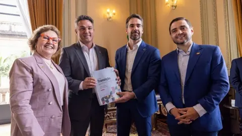 Autoridades posam com um documento de transição em reunião em gabinete oficial.