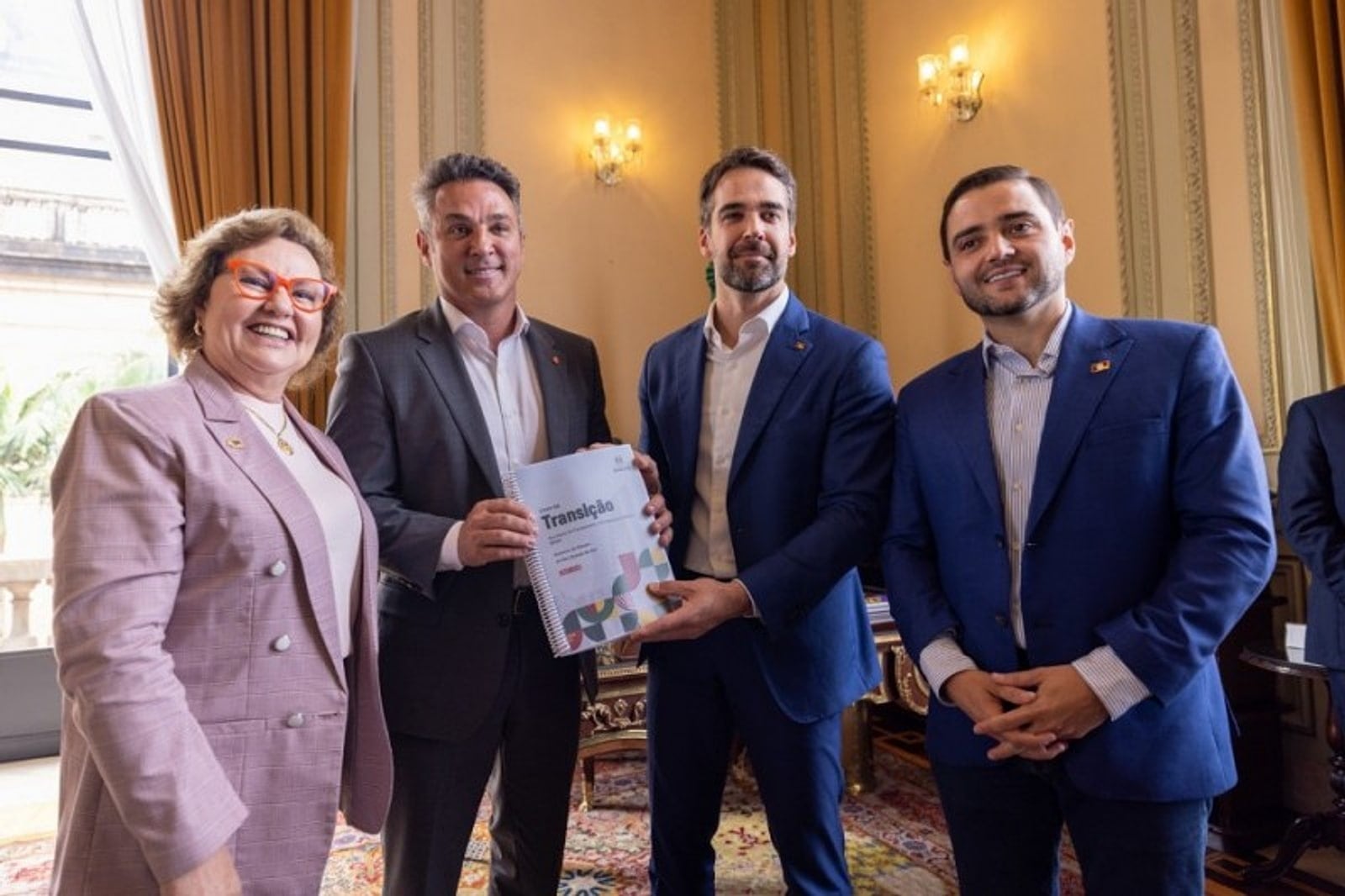 Autoridades posam com um documento de transição em reunião em gabinete oficial.