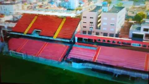 Vista do estádio Bento Freitas, em Pelotas, com arquibancadas vermelhas e prédios ao redor.