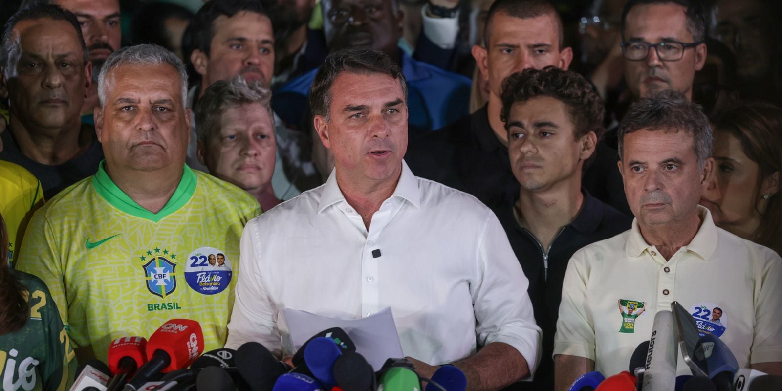 Flávio Bolsonaro fala à imprensa, cercado de apoiadores.