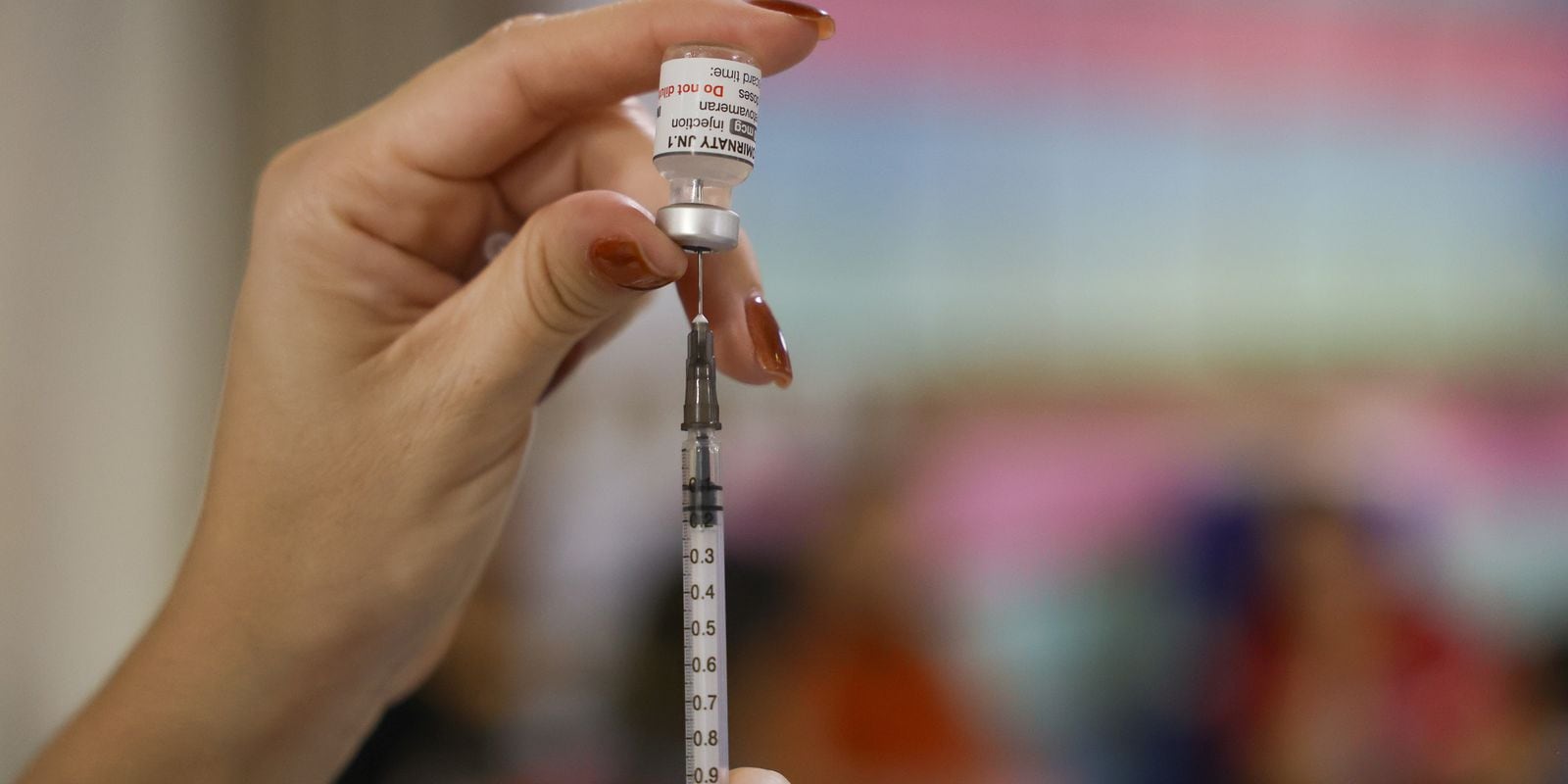 Profissional de saúde prepara dose de vacina em seringa; a cobertura vacinal infantil é o tema da matéria.