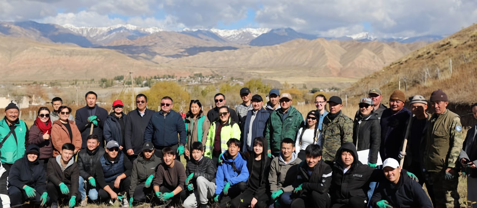 Grupo de pessoas, muitas com luvas verdes, posa em área de plantio com montanhas ao fundo.