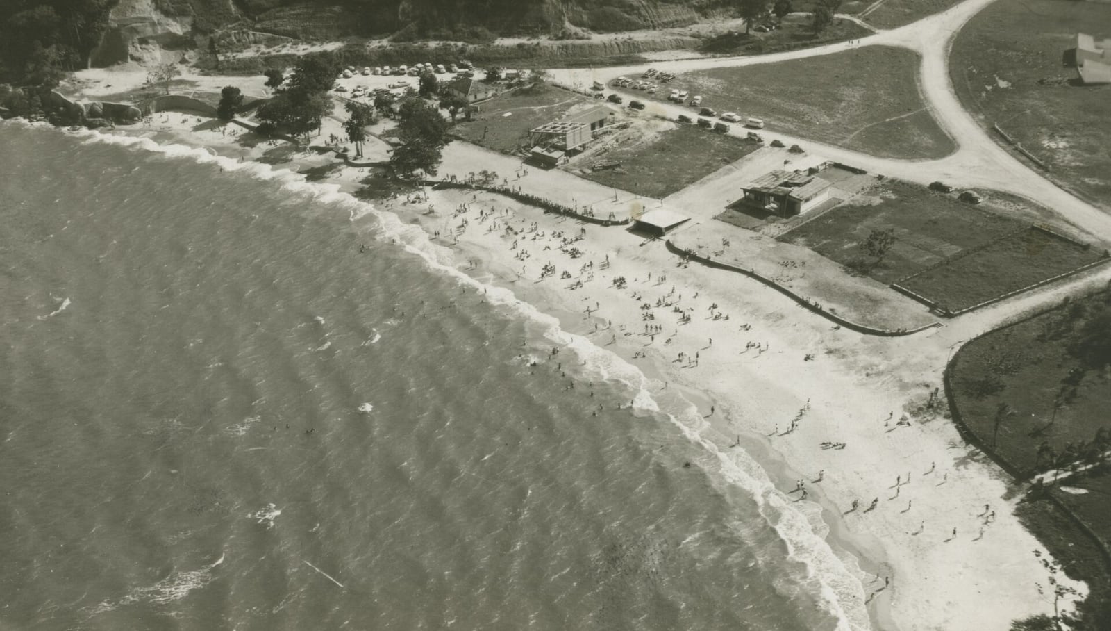 Vista aérea histórica de Caraguatatuba (SP), com banhistas espalhados pela praia.