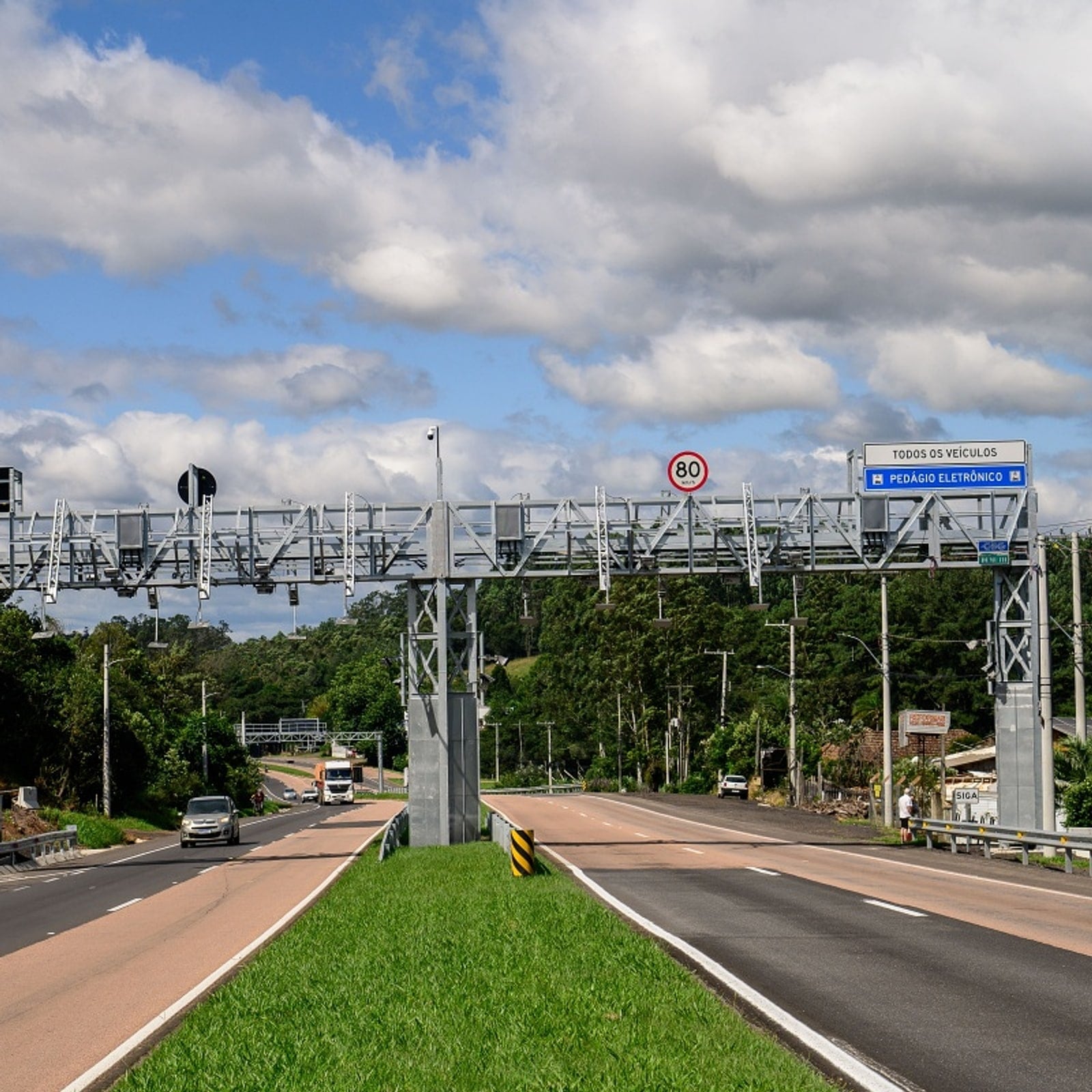 Pórtico do pedágio eletrônico free flow da CSG sobre a rodovia, com placa indicando cobrança para todos os veículos.