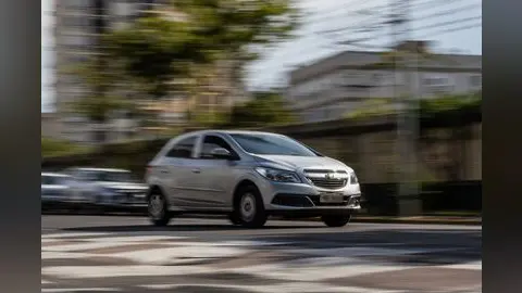 Carro prata em movimento em via urbana, com efeito de borrão que sugere velocidade.