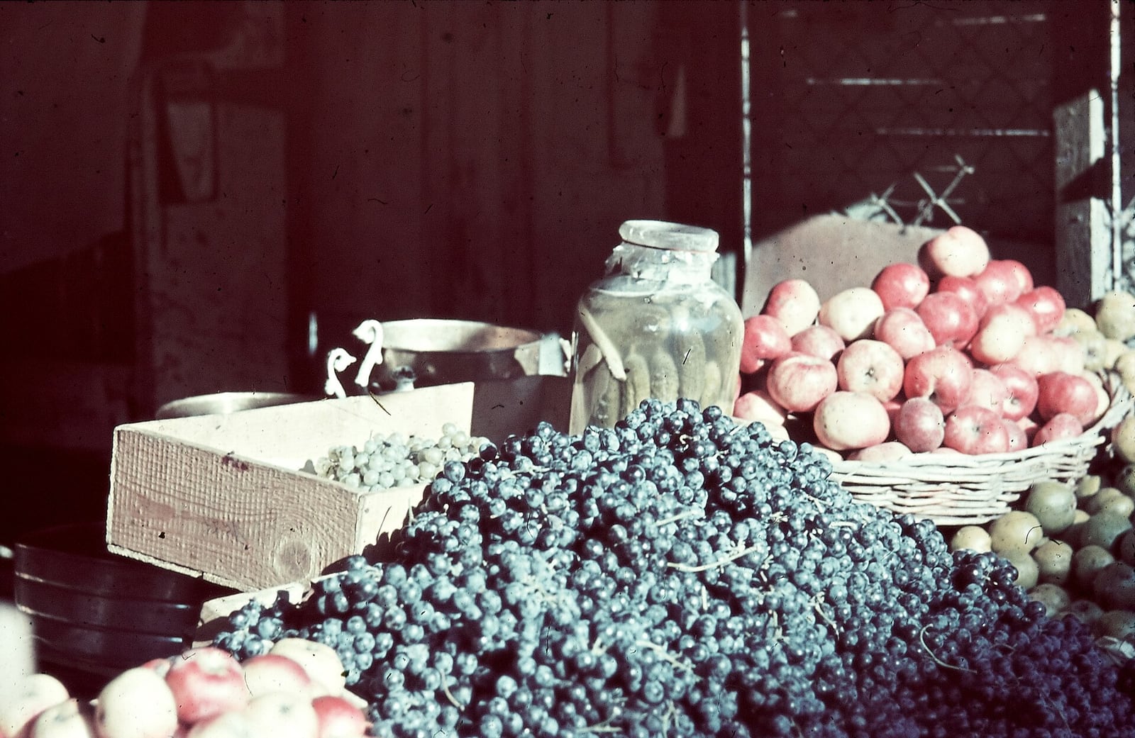 Maçãs vermelhas em cesto e uvas azuis expostas em banca de mercado de frutas.
