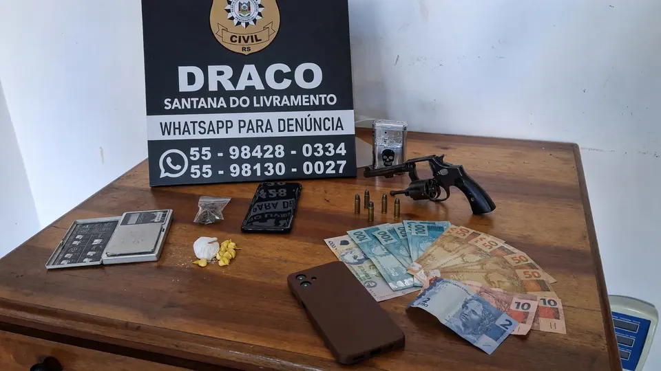 Arma municiada, porções de drogas e cédulas de dinheiro dispostas sobre uma mesa durante apreensão policial
