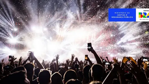 Público em show com celulares erguidos e luzes no palco. Imagem ilustrativa.