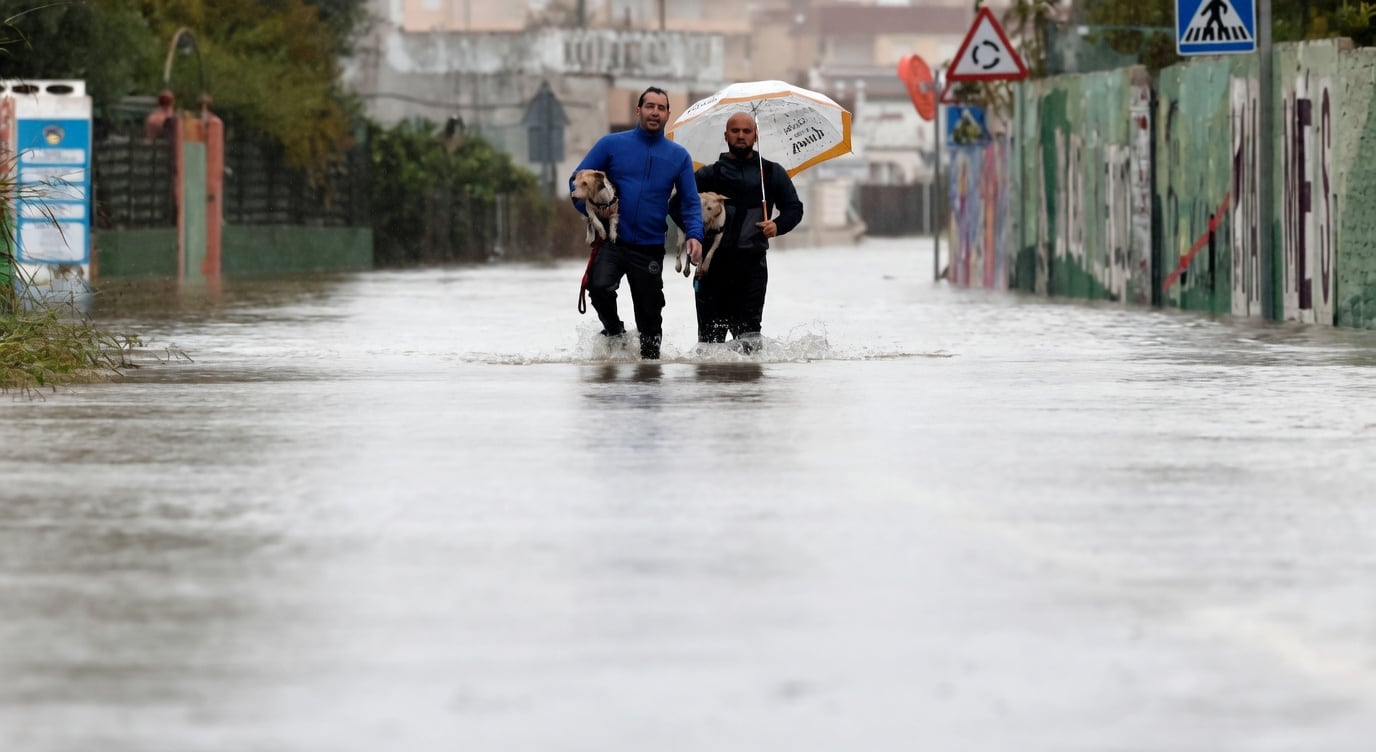 Duas pessoas caminham com cães por uma rua alagada durante a tempestade Adam, na Espanha.
