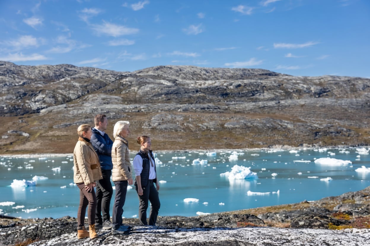 Representantes da União Europeia observam uma paisagem do Ártico, com icebergs flutuando em água azul.